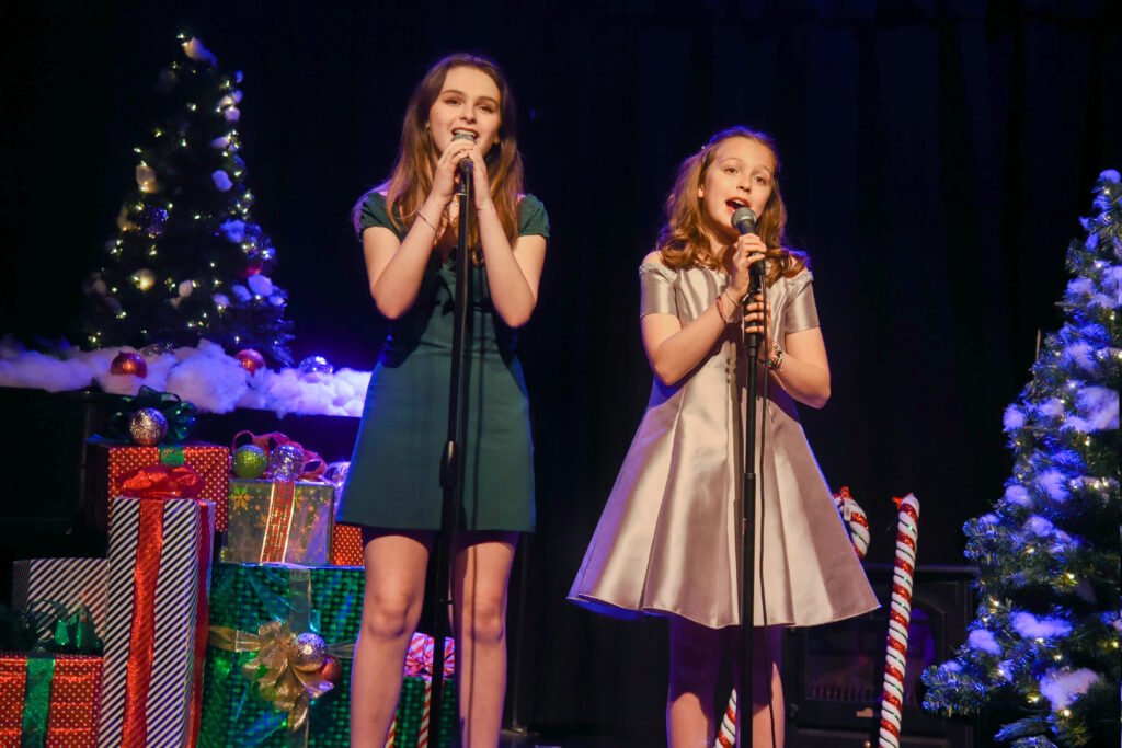 Two young performers singing on a holiday-themed stage.
